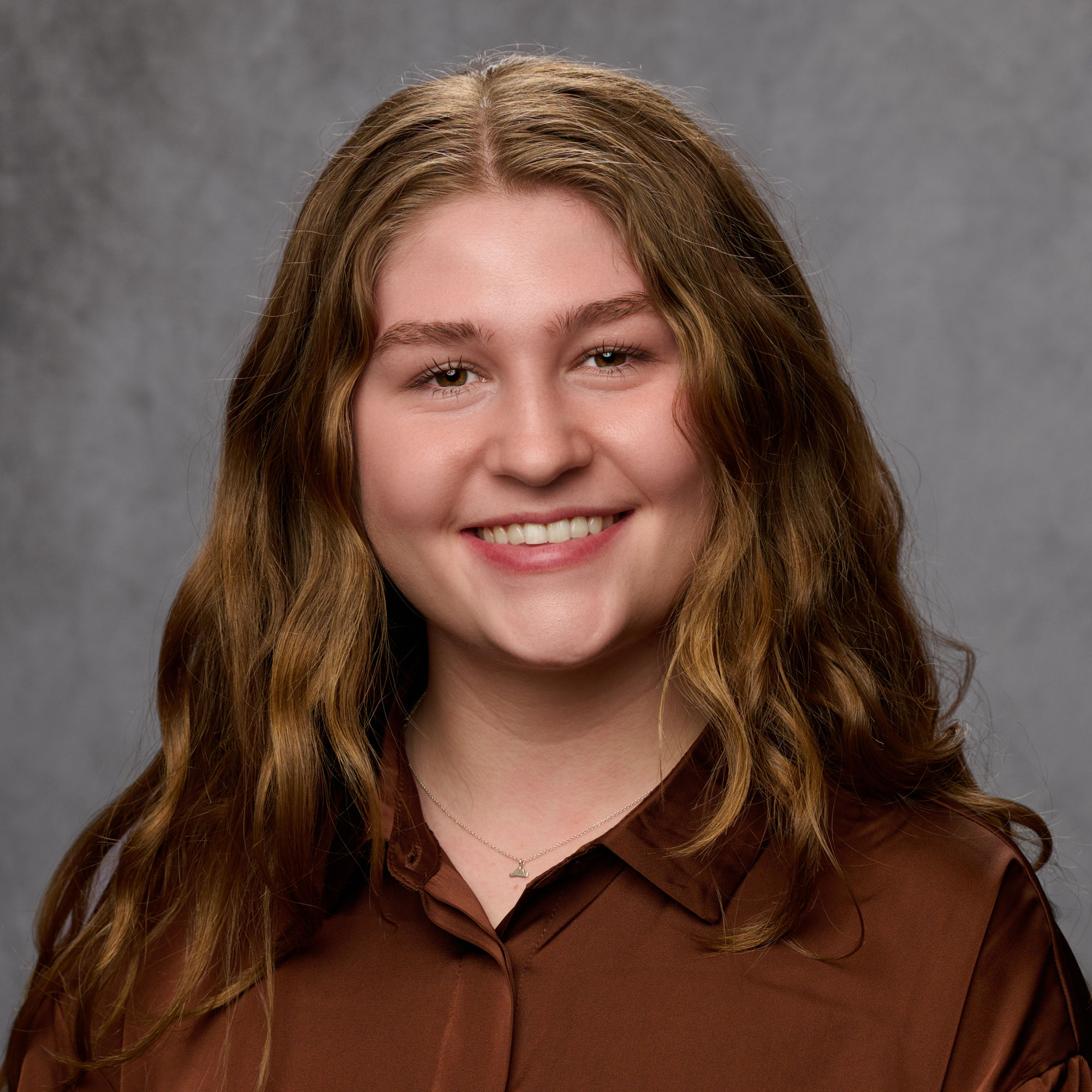 Erika Hochstein smiling in a brown button up with a grey backdrop.